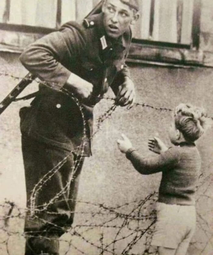 Soldier interacting with a young boy near barbed wire, captured in an antique historical photograph from the past.