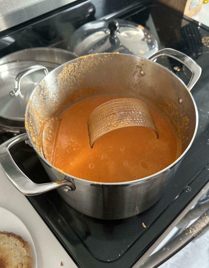 Large pot on stove with a cooking fail showing a broken utensil submerged in thick orange sauce spillover.