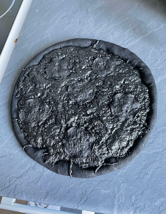 Burnt blackened pizza on a countertop, showing a cooking fail likely from overcooking or improper preparation.