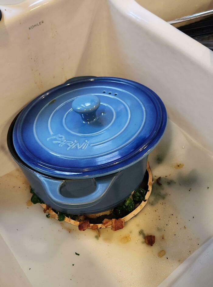 Blue pot stuck in kitchen sink drain with food debris around, illustrating hilariously painful cooking fails.