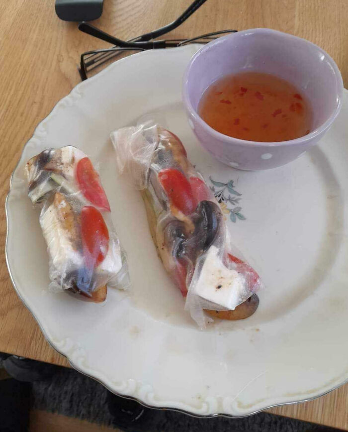 Two poorly wrapped spring rolls on a plate next to a dipping sauce, showing a cooking fail accident.