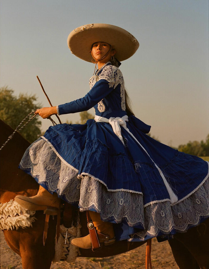 Female rodeo rider in traditional dress and wide-brimmed hat captured riding a horse showcasing power and beauty.