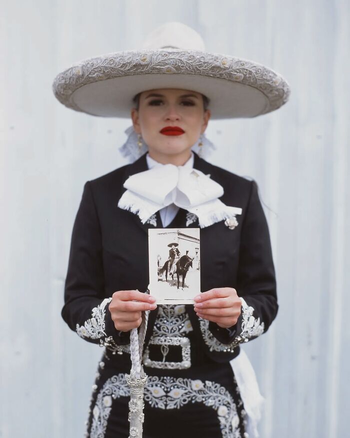 Female rodeo rider dressed in traditional charro attire holding a vintage black-and-white photo of a rider on horseback.