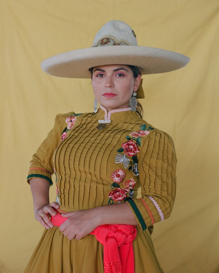 Female rodeo rider wearing traditional embroidered dress and wide-brimmed hat, showcasing beauty and power.