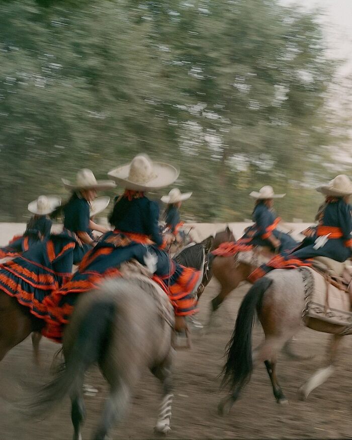 Female rodeo riders wearing traditional dresses and sombreros ride horses in a dynamic all-female rodeo scene.