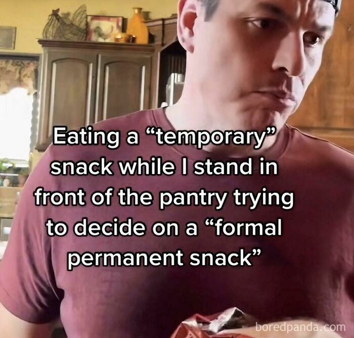 Man in a kitchen eating a "temporary" snack while deciding on a "formal permanent snack," showing relatable human experience.