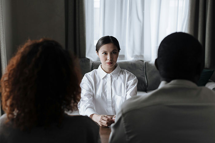 Young woman in white shirt calmly confronting couple in a tense discussion about refusing to invite bully brother to wedding. Young woman in white shirt calmly confronting couple in a tense discussion about refusing to invite bully brother to wedding.