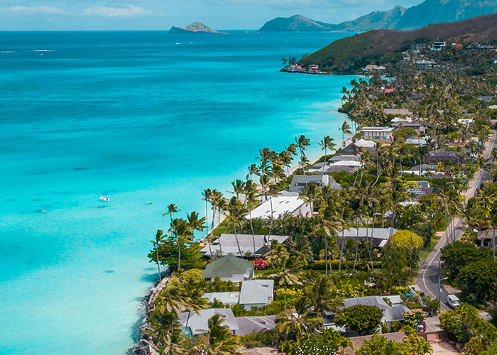 Aerial view of a tropical coastline with clear blue water and residential homes reflecting living in home countries.