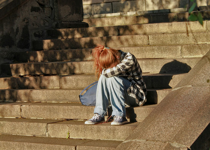 Person sitting on outdoor stone steps with head down, conveying frustration and stress related to things said by people in charge.