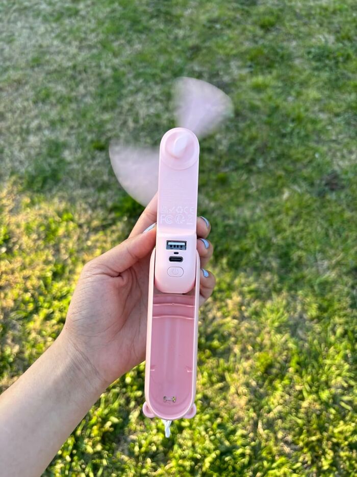 Hand holding a portable pink mini fan with USB charging port, ideal for warm weather finds to stay cool outdoors.