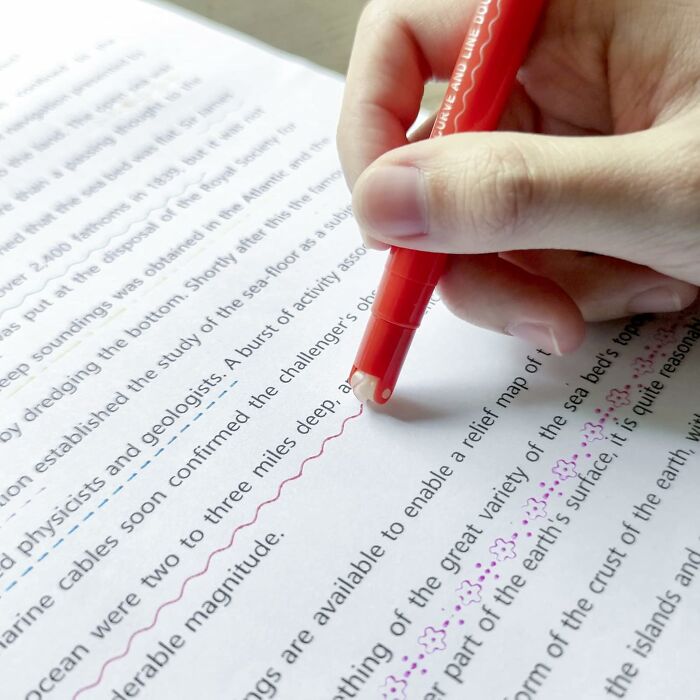 Close-up of hand using a red pen to mark text on paper, highlighting office supplies for an organized desk setup.