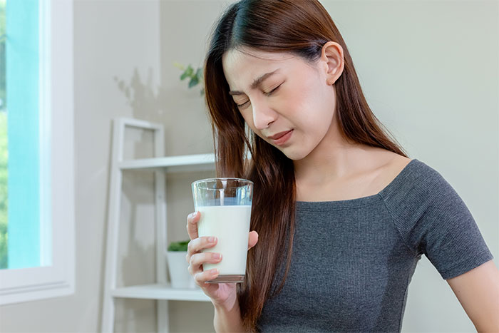 Young woman holding a glass of milk with a disgusted expression reacting to food stolen by roommate. Young woman holding a glass of milk with a disgusted expression reacting to food stolen by roommate.