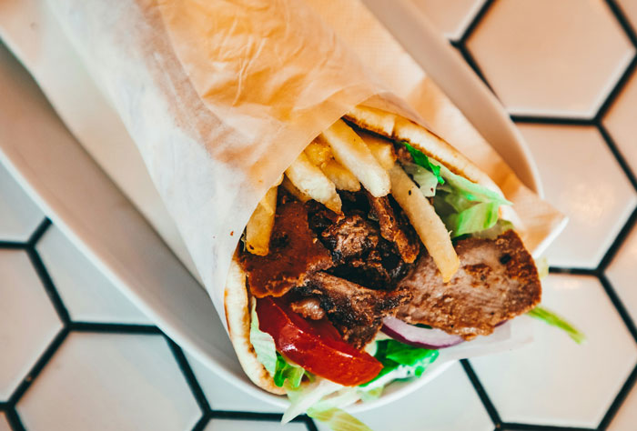 Close-up of a wrapped sandwich with fries, lettuce, and meat on a white hexagonal tile surface, illustrating mug attempts context.