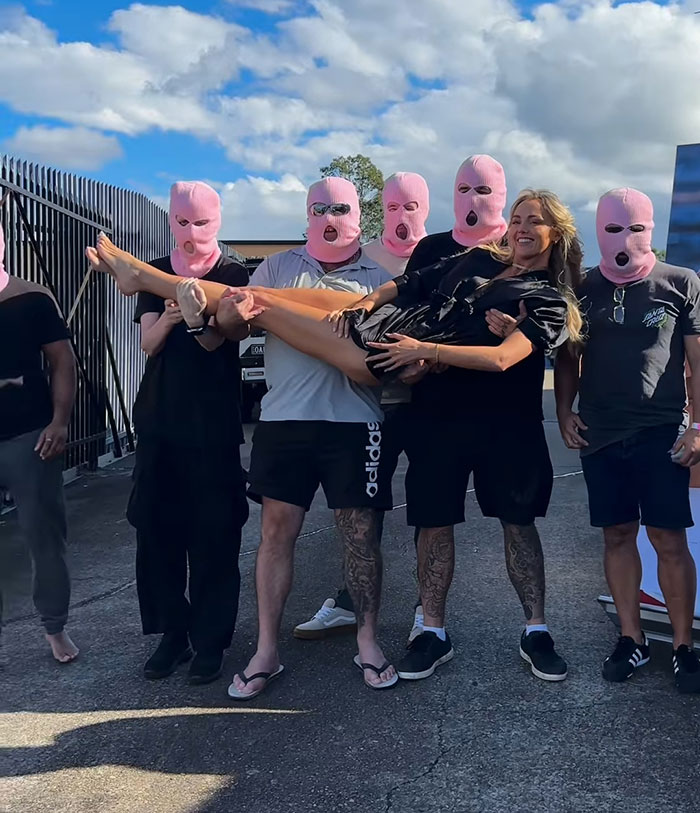 Adult content creator smiling while being held by a group wearing pink masks, linked to bleeding hospital update story. Adult content creator smiling while being held by a group wearing pink masks, linked to bleeding hospital update story.