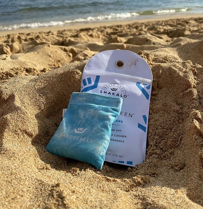Sandscreen beach care product pouch and packaging resting on sand near ocean shore, ideal warm weather find.