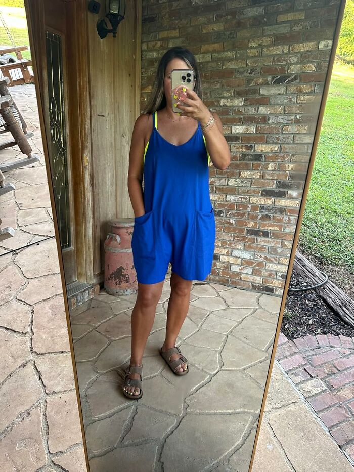 Woman in a blue romper and sandals taking a mirror selfie outdoors showcasing warm weather fashion finds.