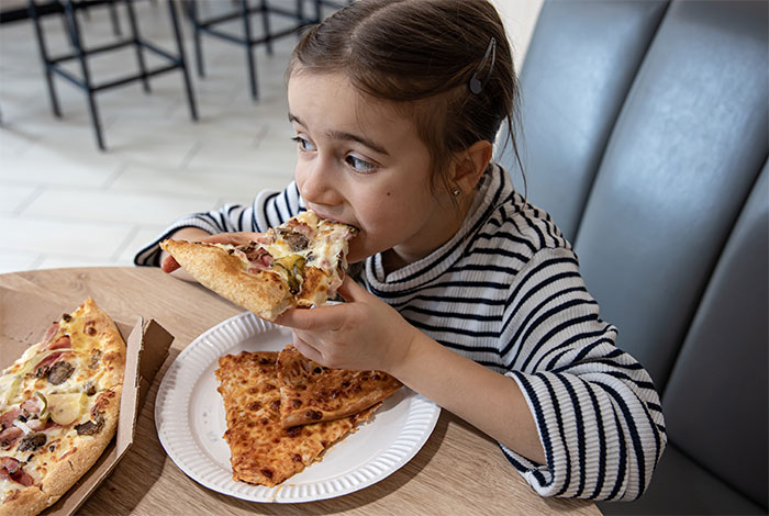 Young girl eating pizza at a table, illustrating a kid outing related to refusing outings with brother’s kids. Young girl eating pizza at a table, illustrating a kid outing related to refusing outings with brother’s kids.