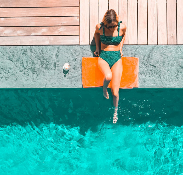 Woman in a green swimsuit relaxing by a pool, reflecting on secrets spouses keep after marriage.