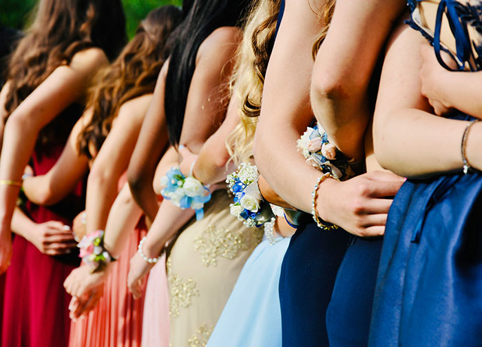 Teen girls dressed for prom stand side by side, wearing corsages and formal gowns in various colors. Teen girls dressed for prom stand side by side, wearing corsages and formal gowns in various colors.