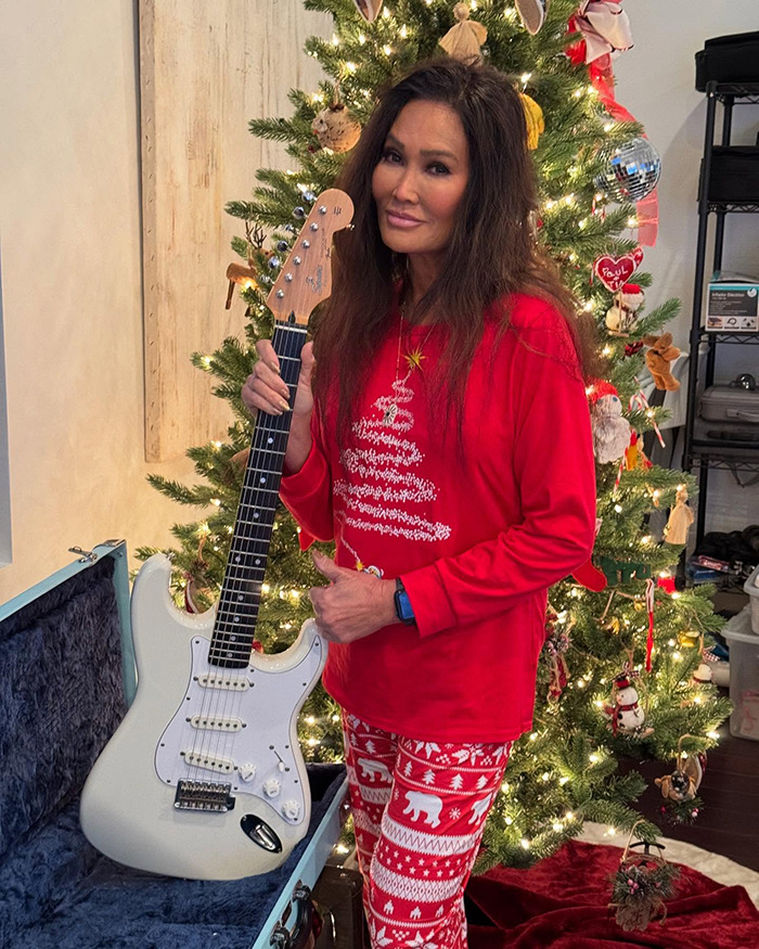 Tia Carrere, 90s icon, posing with guitar in festive red holiday outfit near decorated Christmas tree. Tia Carrere, 90s icon, posing with guitar in festive red holiday outfit near decorated Christmas tree.