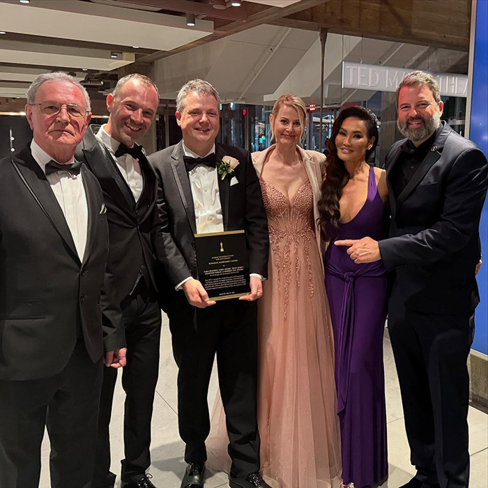 Tia Carrere in a plunging purple gown posing with five people at an event, showcasing her timeless '90s icon style. Tia Carrere in a plunging purple gown posing with five people at an event, showcasing her timeless '90s icon style.