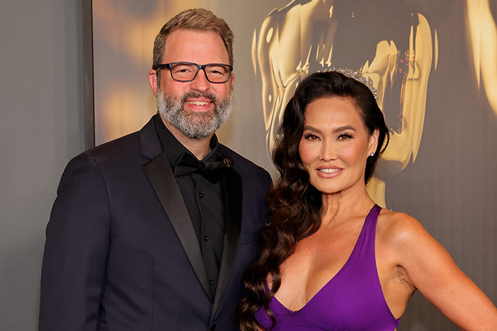 Tia Carrere in a plunging purple gown posing with a man in a black suit at a formal event. Tia Carrere in a plunging purple gown posing with a man in a black suit at a formal event.
