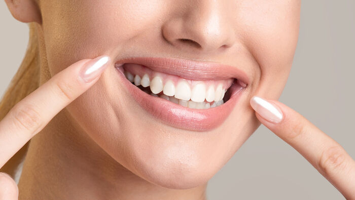 Close-up of a smiling woman pointing to her teeth, highlighting the concept of Ozempic teeth side effects from weight loss meds. Close-up of a smiling woman pointing to her teeth, highlighting the concept of Ozempic teeth side effects from weight loss meds.