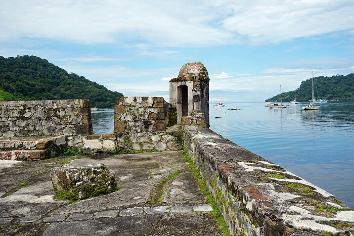 Ancient stone fort ruins by calm water with boats and green hills, illustrating bizarre historical events.