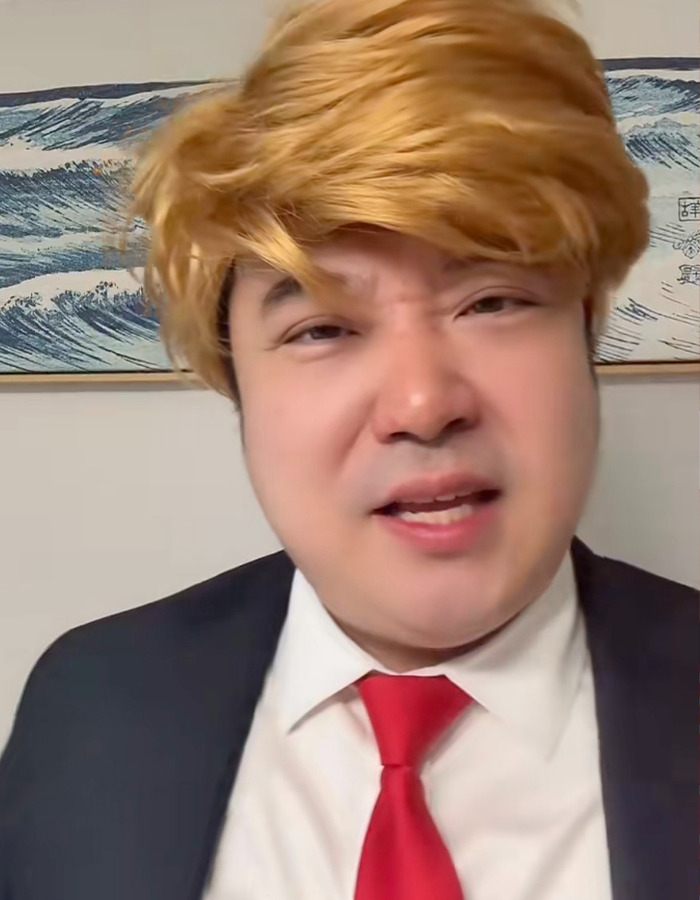 Chinese TikToker dressed as U.S. president with blond wig and red tie, performing viral impression in front of wave artwork. Chinese TikToker dressed as U.S. president with blond wig and red tie, performing viral impression in front of wave artwork.