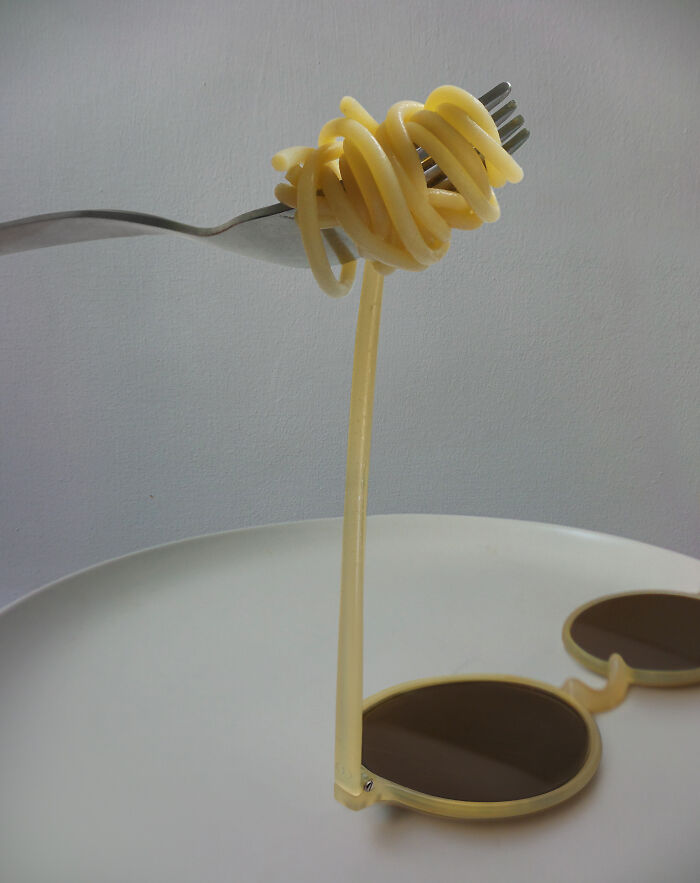 Surreal photo manipulation of spaghetti twisting around a fork with one strand extending to sunglasses on a table.