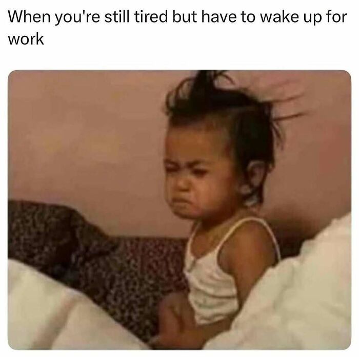 Tired child with messy hair sitting up in bed, capturing relatable memes for those who could use a chuckle today.