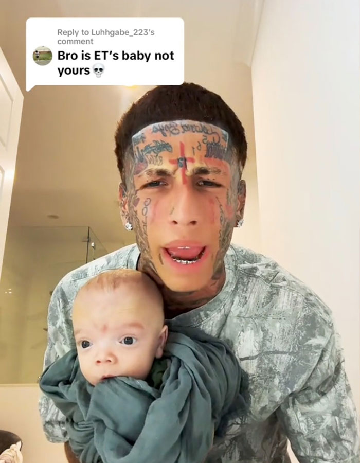 Island Boy with extensive face tattoos holding ET's baby wrapped in a blanket, addressing fans in a video. Island Boy with extensive face tattoos holding ET's baby wrapped in a blanket, addressing fans in a video.