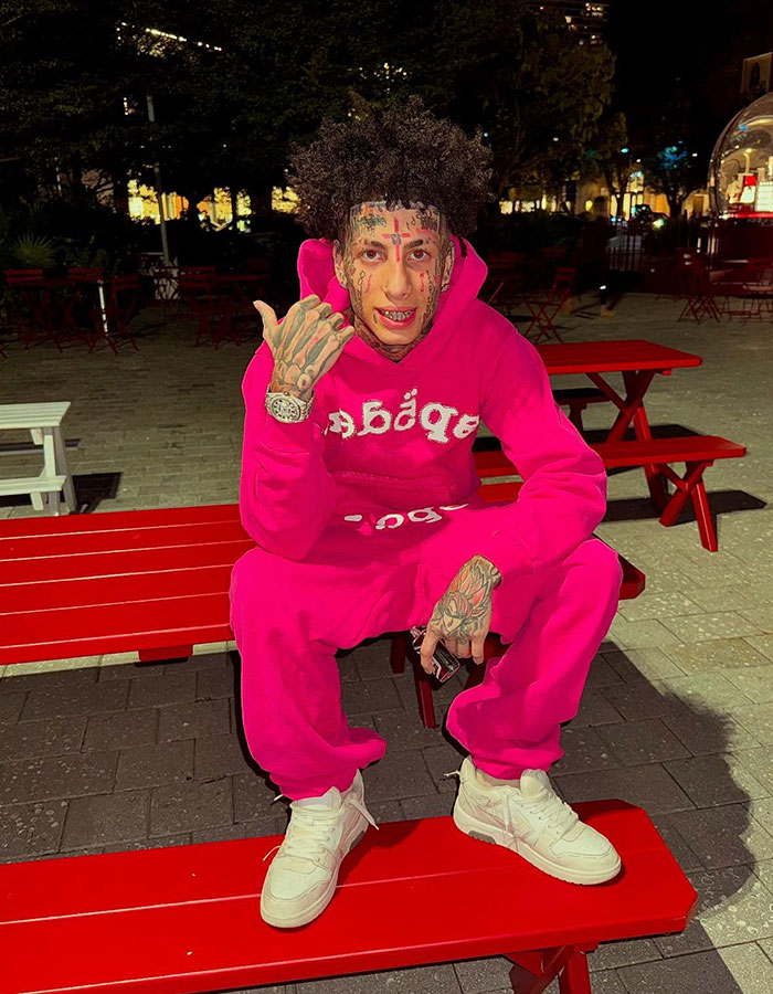 Island boy sitting on red bench at night, wearing bright pink outfit and showing tattoos on face and hands. Island boy sitting on red bench at night, wearing bright pink outfit and showing tattoos on face and hands.