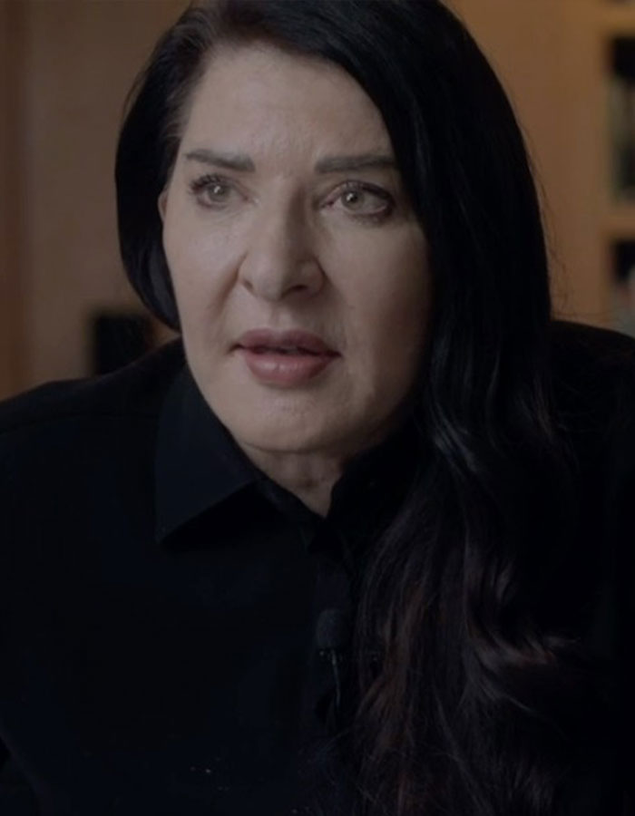 Controversial artist with long dark hair in a black shirt discussing public gallery experience in an indoor setting Controversial artist with long dark hair in a black shirt discussing public gallery experience in an indoor setting