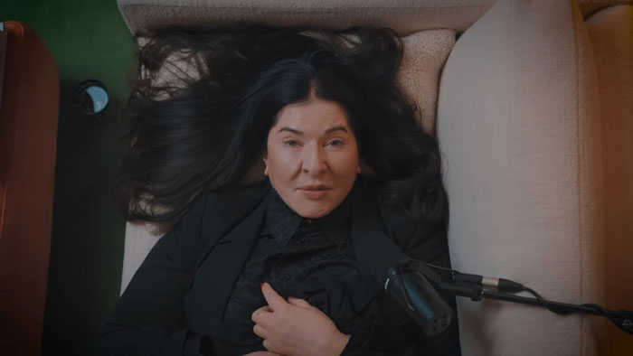 Controversial artist with long black hair lying on couch in black outfit during an interview with a microphone. Controversial artist with long black hair lying on couch in black outfit during an interview with a microphone.
