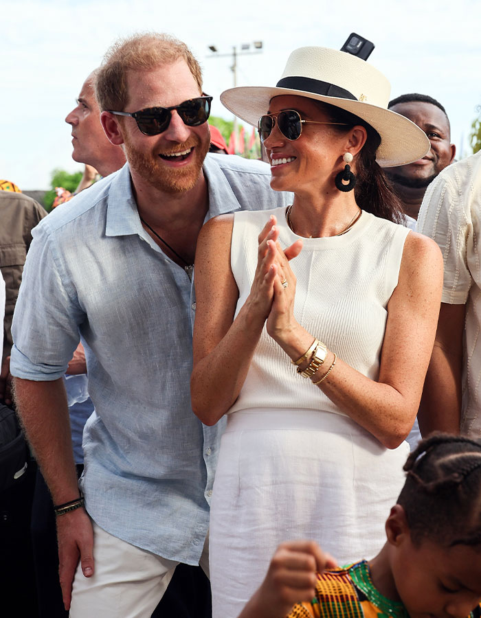 Meghan Markle wearing sunglasses and a hat smiling with Prince Harry outdoors in a candid moment near Montecito. Meghan Markle wearing sunglasses and a hat smiling with Prince Harry outdoors in a candid moment near Montecito.