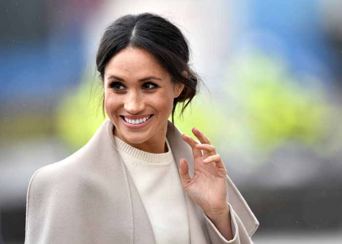 Meghan Markle smiling outdoors wearing a beige coat and white top with blurred background in a very controlled image setting Meghan Markle smiling outdoors wearing a beige coat and white top with blurred background in a very controlled image setting