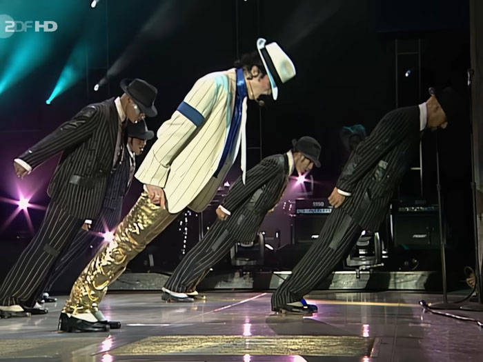 Michael Jackson performing his iconic lean move on stage with backup dancers in pinstripe suits and hats. Michael Jackson performing his iconic lean move on stage with backup dancers in pinstripe suits and hats.