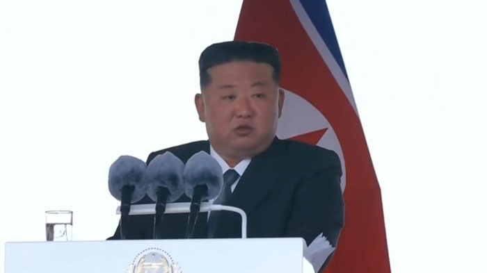 Kim Jong-Un speaking at a podium with North Korean flag behind him, reacting to 5,000-ton warship capsizing event. Kim Jong-Un speaking at a podium with North Korean flag behind him, reacting to 5,000-ton warship capsizing event.