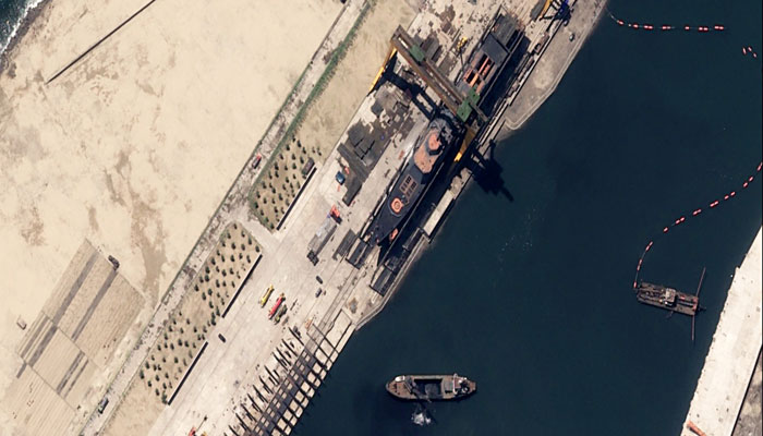 Aerial view of a 5,000-ton warship capsizing at a dock with nearby boats and industrial equipment. Aerial view of a 5,000-ton warship capsizing at a dock with nearby boats and industrial equipment.