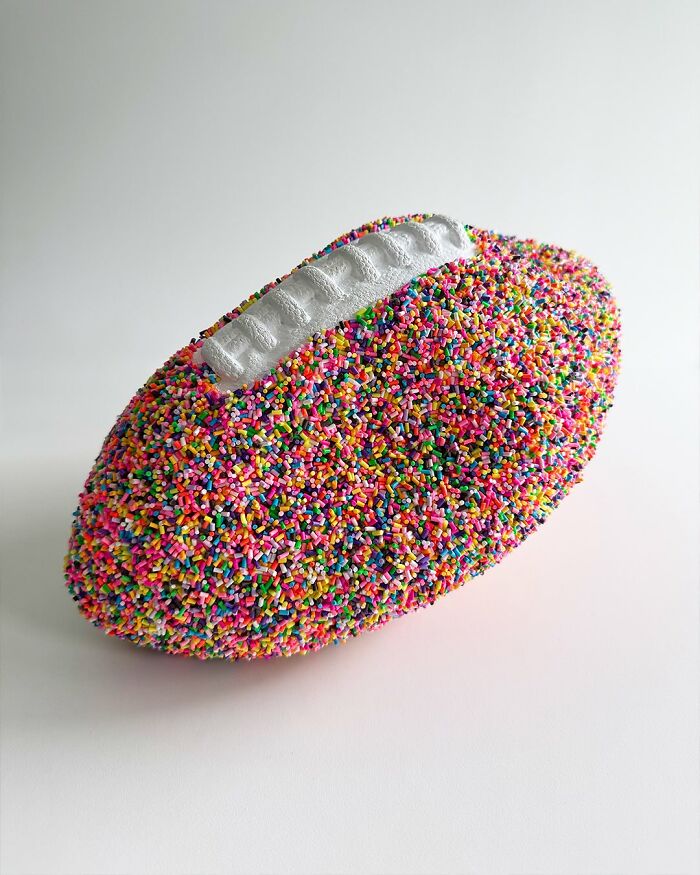 Colorful artwork of a football completely covered in multicolored sprinkles on a white background.