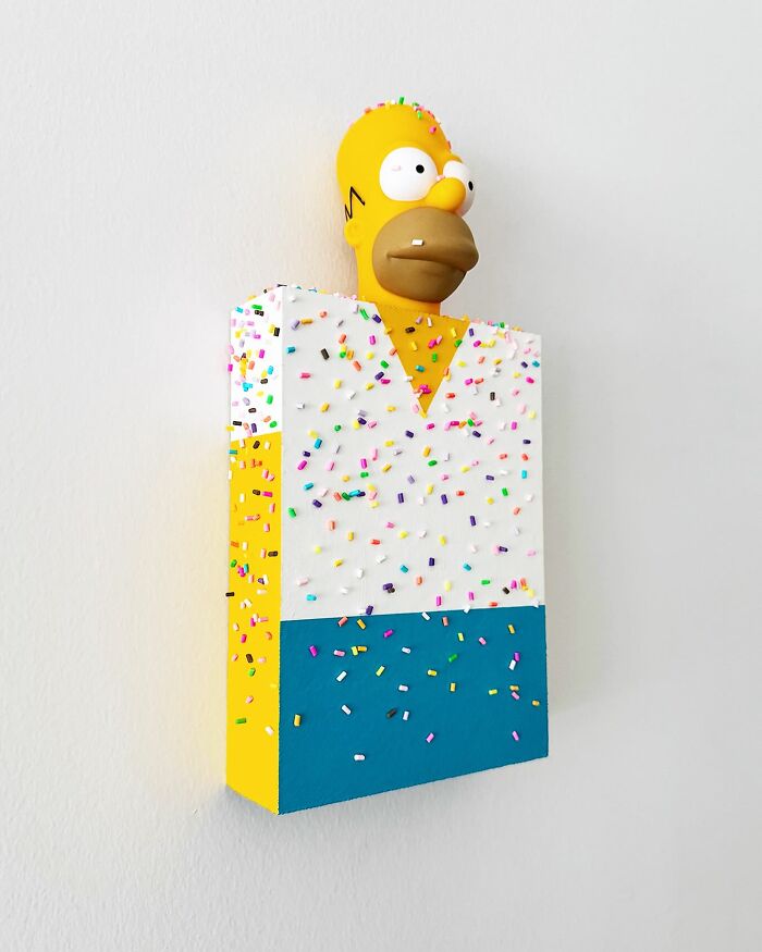 Yellow Homer Simpson figure covered in colorful sprinkles as unique artwork by Pepe Bratanov on a white wall background.