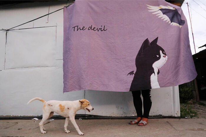 Dog walking on a street beside a person holding a large cloth with a dog illustration, capturing dogs owning the streets.