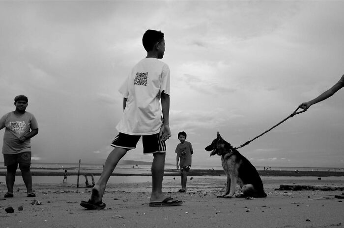 Black and white photo of children on a beach with a dog on a leash capturing dogs owning the streets.
