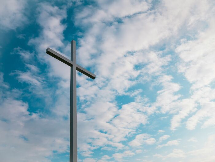 Tall cross against a blue sky with clouds, symbolizing one of the mind-boggling beliefs smart people still stand behind.