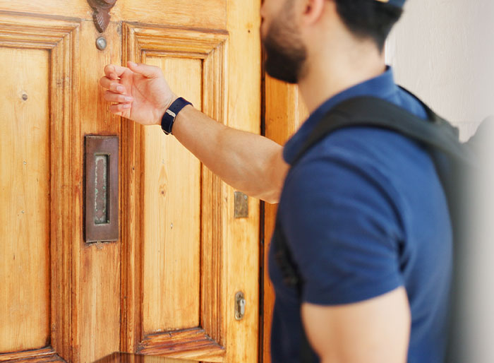 Man wearing blue shirt and backpack knocking on wooden door, illustrating petty revenge after Airbnb price hike attempt. Man wearing blue shirt and backpack knocking on wooden door, illustrating petty revenge after Airbnb price hike attempt.