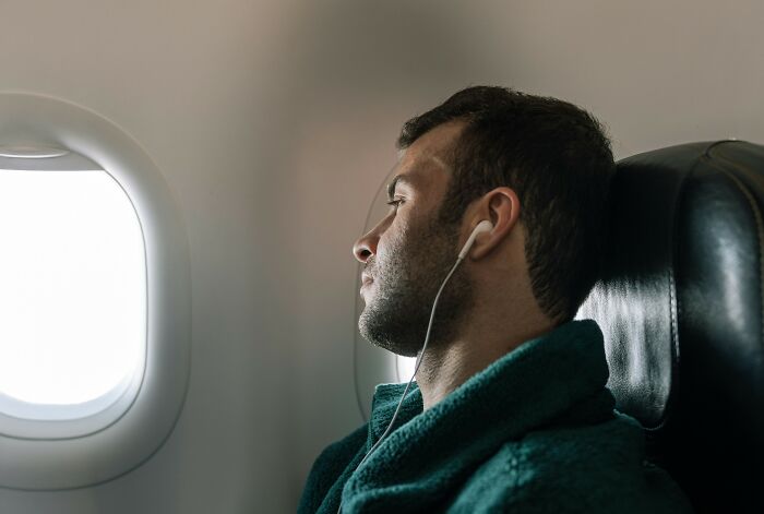 Man wearing earphones sitting by airplane window, enjoying a tiny thing that made the trip better during flight.