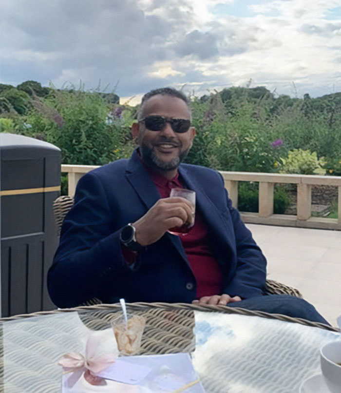 Man in sunglasses and navy blazer sitting outdoors holding a drink, related to father of four with 37 followers jailed over tweet. Man in sunglasses and navy blazer sitting outdoors holding a drink, related to father of four with 37 followers jailed over tweet.