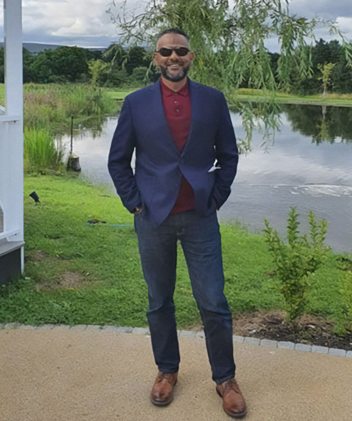 Man standing outdoors near pond, wearing sunglasses and navy blazer, representing father of four with 37 followers jailed over deleted tweet Man standing outdoors near pond, wearing sunglasses and navy blazer, representing father of four with 37 followers jailed over deleted tweet