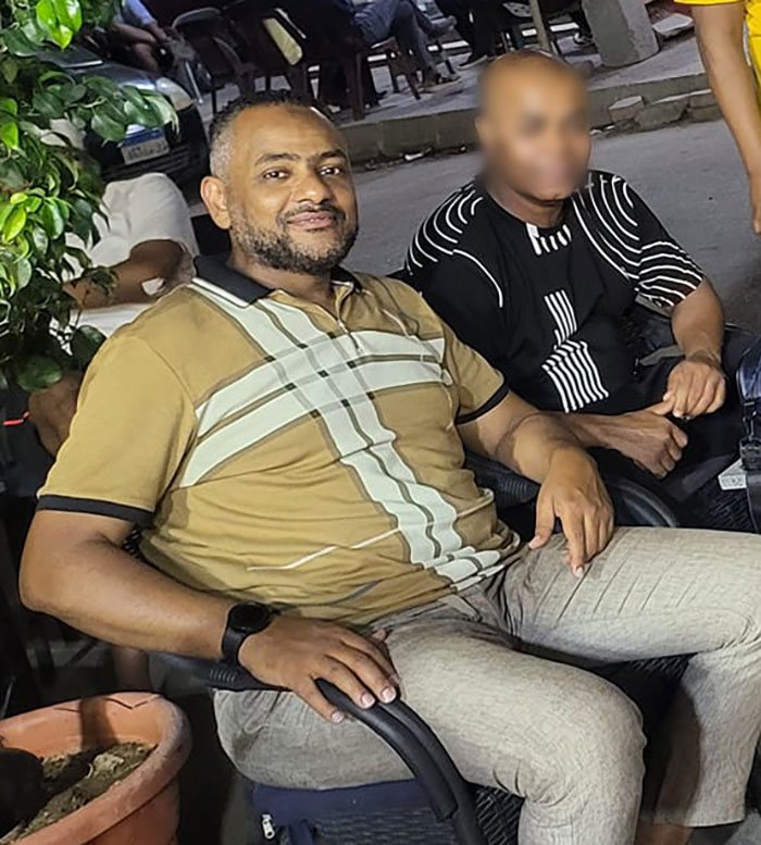 Man sitting outdoors wearing a tan shirt and gray pants, representing father of four with only 37 followers jailed over deleted tweet. Man sitting outdoors wearing a tan shirt and gray pants, representing father of four with only 37 followers jailed over deleted tweet.